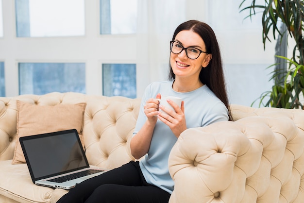 Mujer sentada con café y laptop en sofá