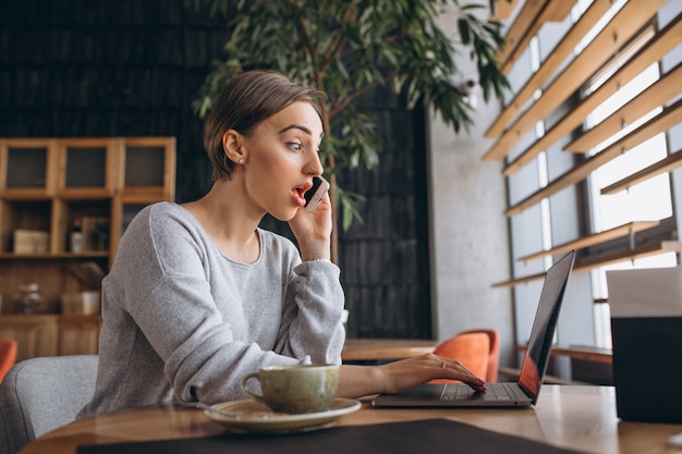 Mujer sentada en un café tomando café y trabajando en una computadora