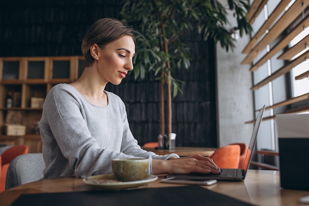 Mujer sentada en un café tomando café y trabajando en una computadora