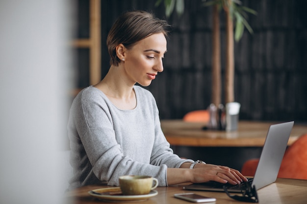 Mujer sentada en un café tomando café y trabajando en una computadora