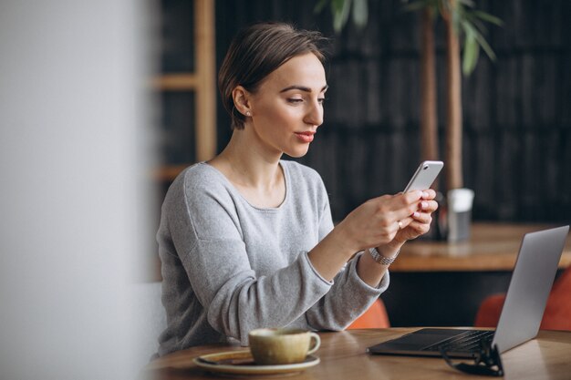 Mujer sentada en un café tomando café y trabajando en una computadora