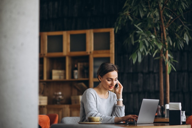 Mujer sentada en un café tomando café y trabajando en una computadora