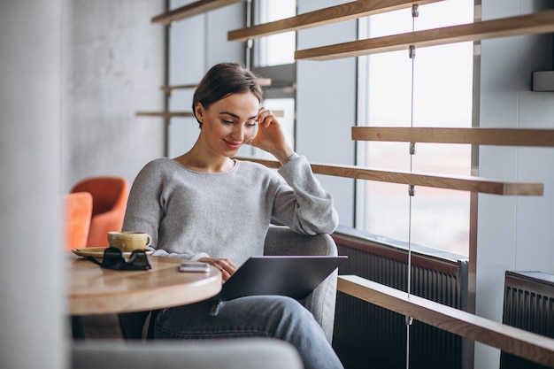 Mujer sentada en un café tomando café y trabajando en una computadora