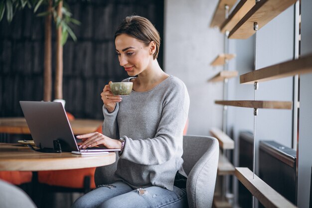 Mujer sentada en un café tomando café y trabajando en una computadora