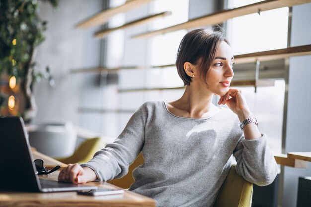 Mujer sentada en un café tomando café y trabajando en una computadora