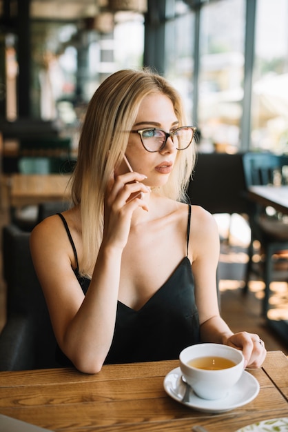 Mujer sentada en la cafetería hablando por teléfono móvil mirando a otro lado