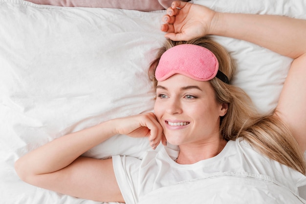 Foto gratuita mujer sentada en la cama con antifaz para dormir