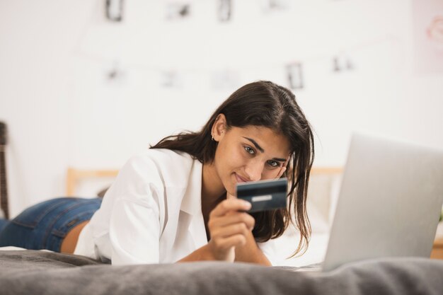Mujer sentada en la cama y mirando una tarjeta de crédito