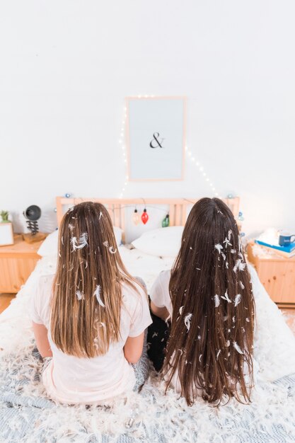 Mujer sentada en la cama con plumas blancas sobre el cabello