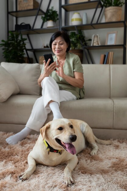 Mujer sentada en casa en un sofá usando un teléfono inteligente al lado de su perro