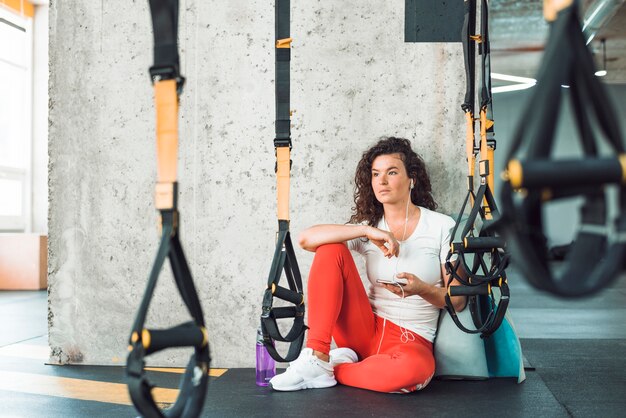 Mujer sentada cerca de la correa de fitness escuchando música en el teléfono móvil