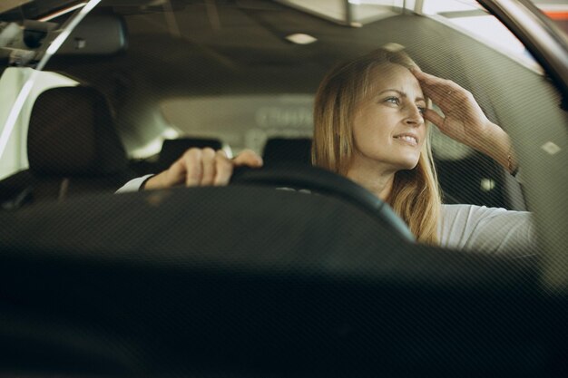 Mujer sentada en el coche nuevo hee en un salón de autos