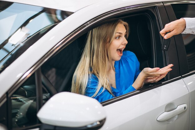 Mujer sentada en el coche y recibir las llaves en una sala de exposición de automóviles