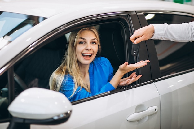 Mujer sentada en el coche y recibir las llaves en una sala de exposición de automóviles
