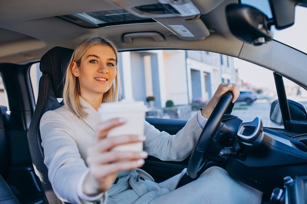 Mujer sentada dentro del auto eléctrico mientras carga con una taza de café