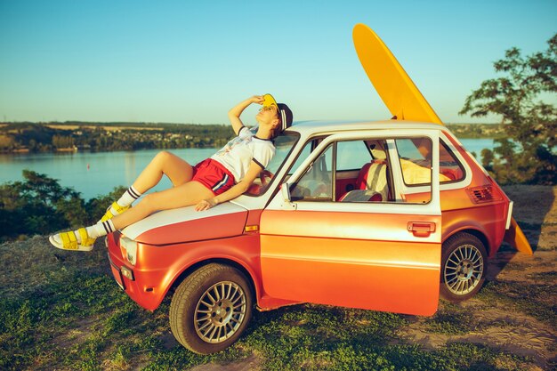 Mujer sentada y descansando en el coche en la playa en un día de verano cerca del río.