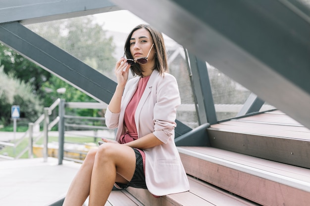 Mujer sentada en la escalera quitando las gafas de sol