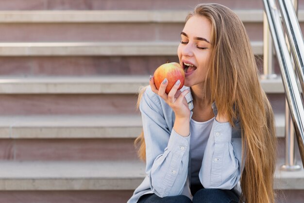 Mujer sentada en las escaleras y comiendo una manzana