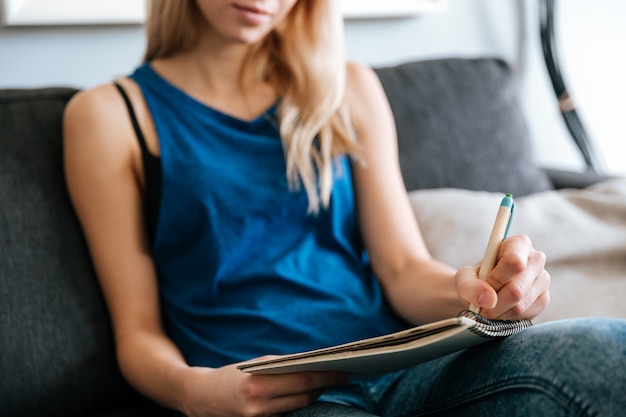 Mujer sentada y escribiendo en el bloc de notas en casa