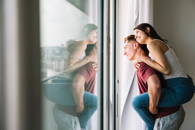 Mujer sentada en la espalda del hombre y mirando a la ventana