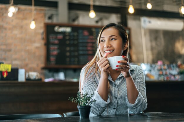 Mujer sentada felizmente tomando café en la cafetería