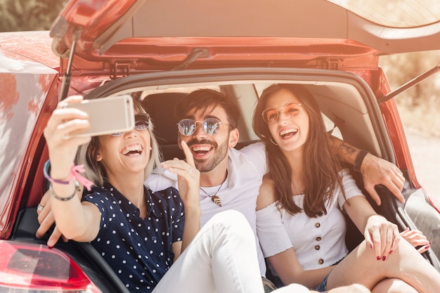 Foto gratuita mujer sentada en la fotografía de toma de tronco de coche a través de teléfono móvil