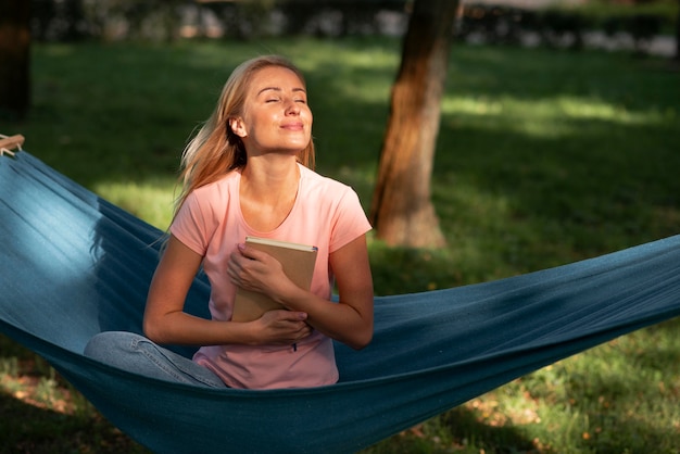 Foto gratuita mujer sentada en una hamaca y sosteniendo un libro