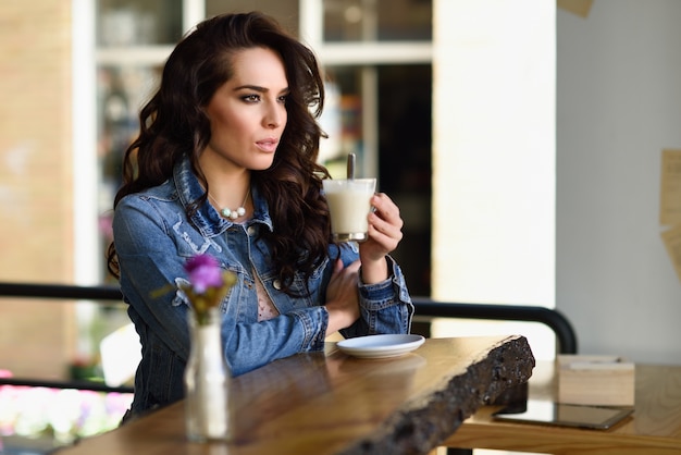 Mujer sentada en el interior de café urbano mirando a través de la ventana