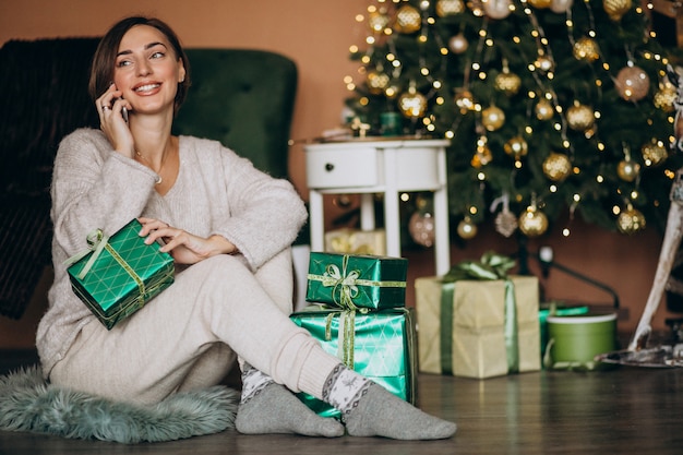 Mujer sentada junto al árbol de Navidad y de compras por teléfono