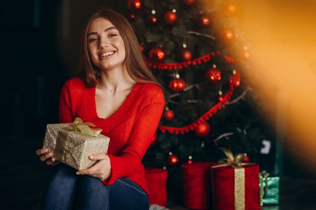 Mujer sentada junto al árbol de Navidad y desempacando el regalo de Navidad