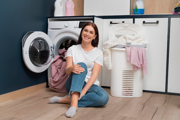 Mujer sentada junto a la lavadora con una canasta llena de ropa