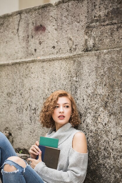 Mujer sentada junto a la pared de piedra y sosteniendo cuadernos