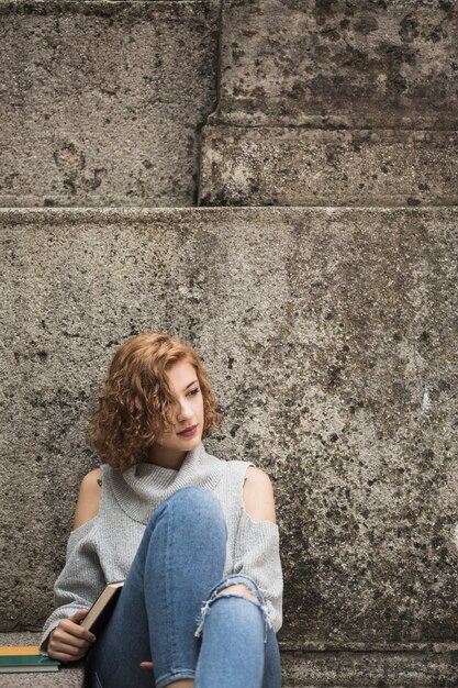 Mujer sentada junto a la pared de piedra