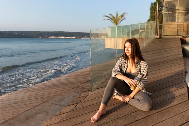 Mujer sentada junto a la playa con espacio de copia