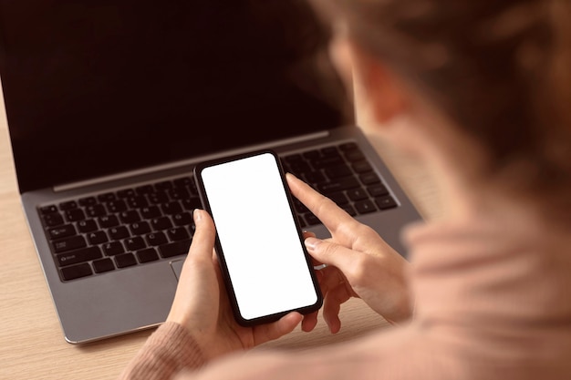 Mujer sentada junto a su computadora portátil y con smartphone