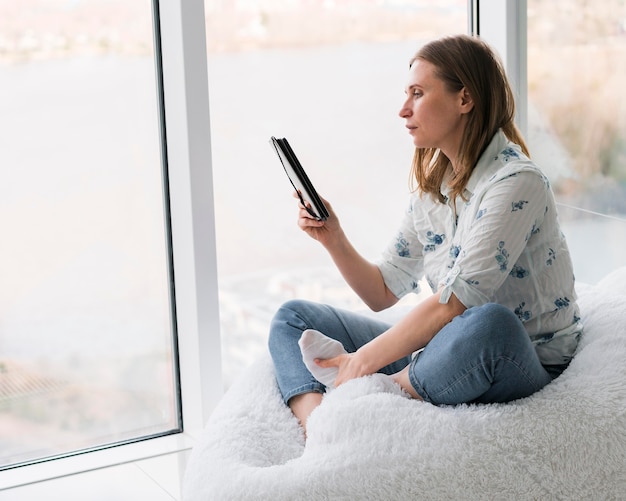 Foto gratuita mujer sentada junto a la ventana con su teléfono