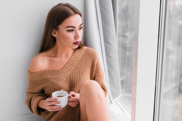 Foto gratuita mujer sentada junto a las ventanas y tomando café