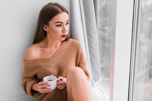 Mujer sentada junto a las ventanas y tomando café