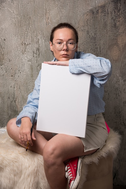 Mujer sentada con lienzo en blanco vacío y pincel sobre fondo de mármol.