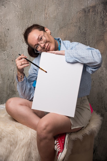 Foto gratuita mujer sentada con lienzo y pincel sobre fondo de mármol.