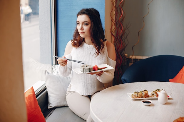 Mujer sentada en la mesa y comiendo sushi en la cafetería