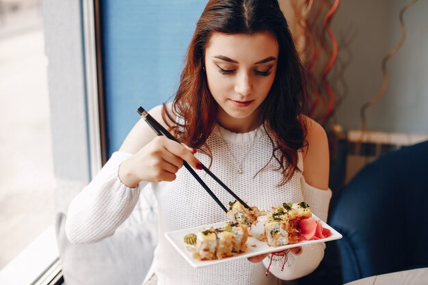 Mujer sentada en la mesa y comiendo sushi en la cafetería