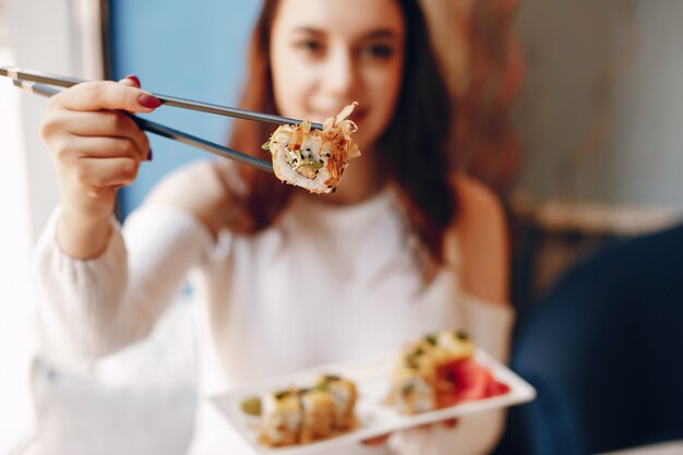 Mujer sentada en la mesa y comiendo sushi en la cafetería