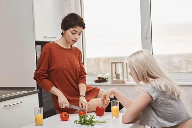 Mujer sentada en la mesa cortando tomotoes mientras su amiga bebe jugo de naranja