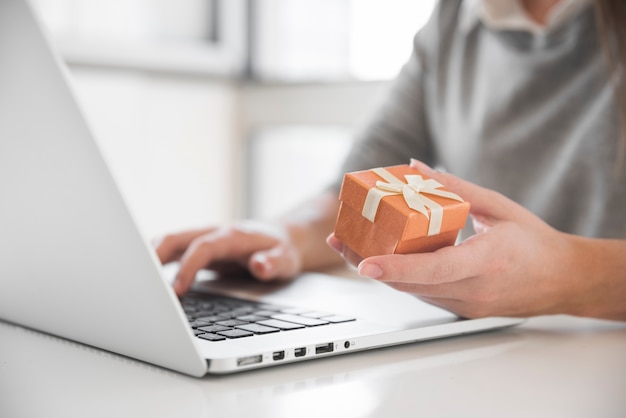 Mujer sentada a la mesa con laptop y caja de regalo