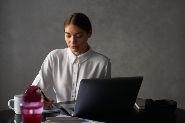 Mujer sentada en la mesa con laptop y escribiendo notas