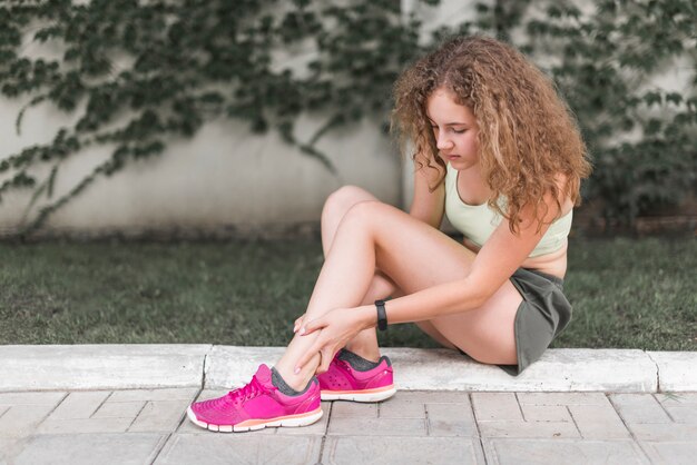 Mujer sentada en el parque mirando el tobillo lesionado