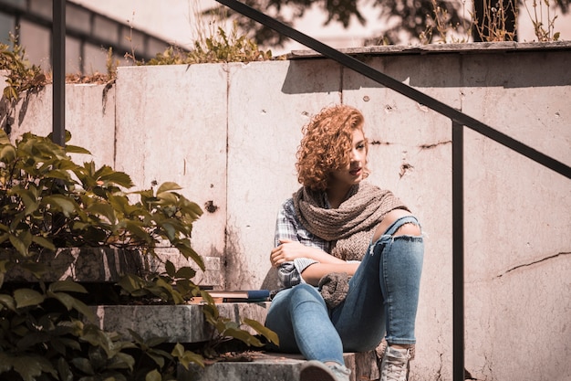 Mujer sentada en pasos cerca de libros en jardín público