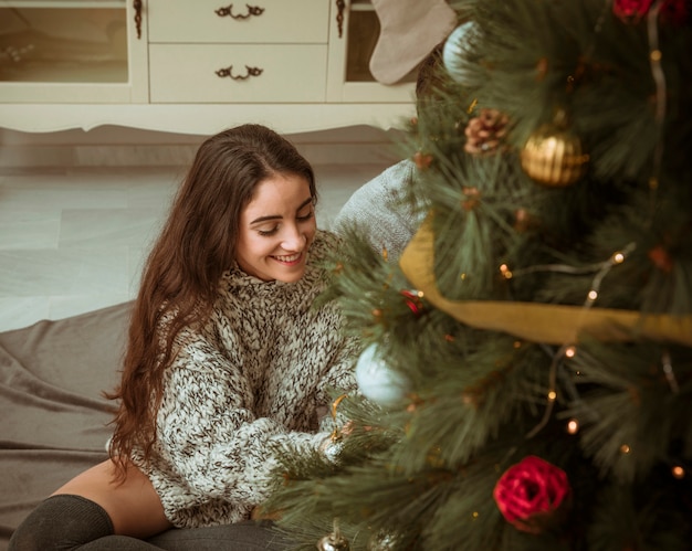 Mujer sentada en el piso y decorando el árbol de navidad