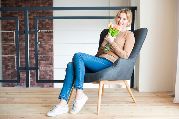 Mujer sentada con ramo de tulipanes en sillón